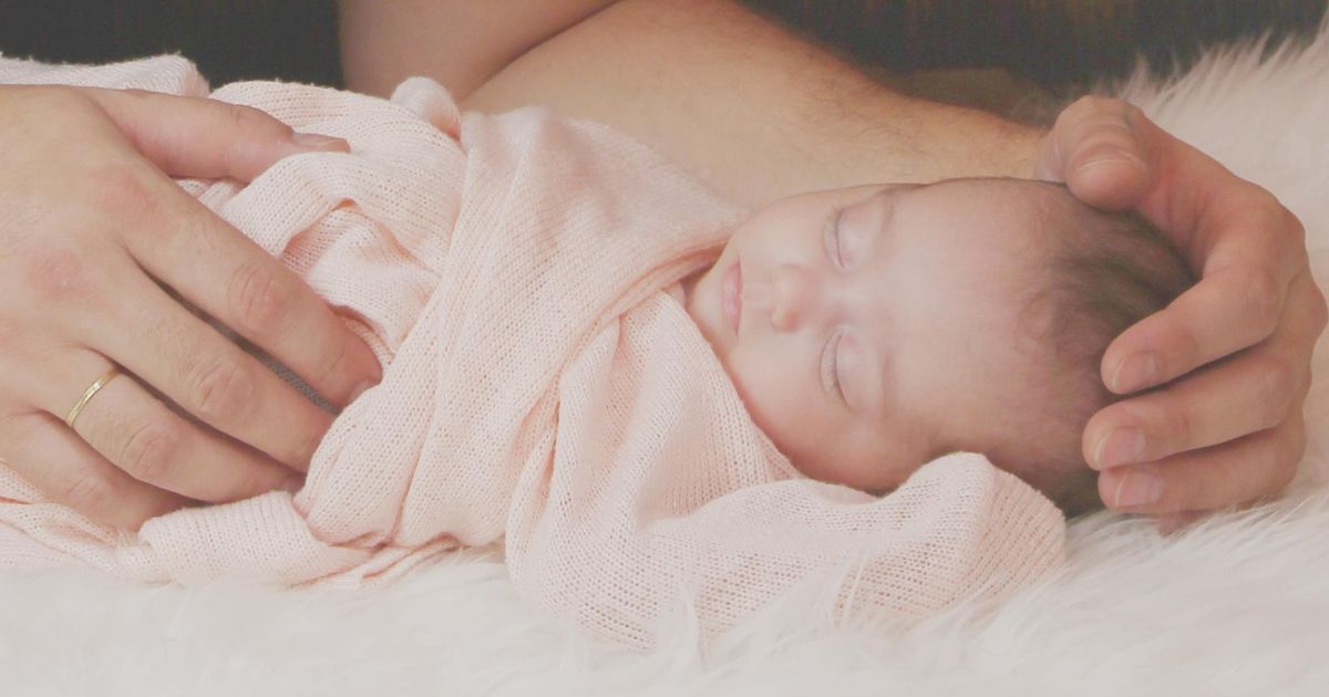 A woman is holding a newborn baby wrapped in a pink blanket.