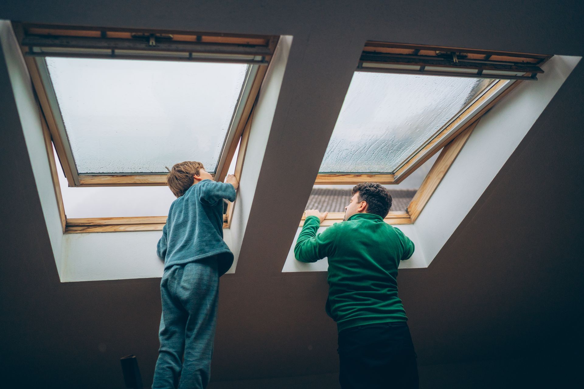 Father and son working together to open skylights in a cosy home on a rainy day.