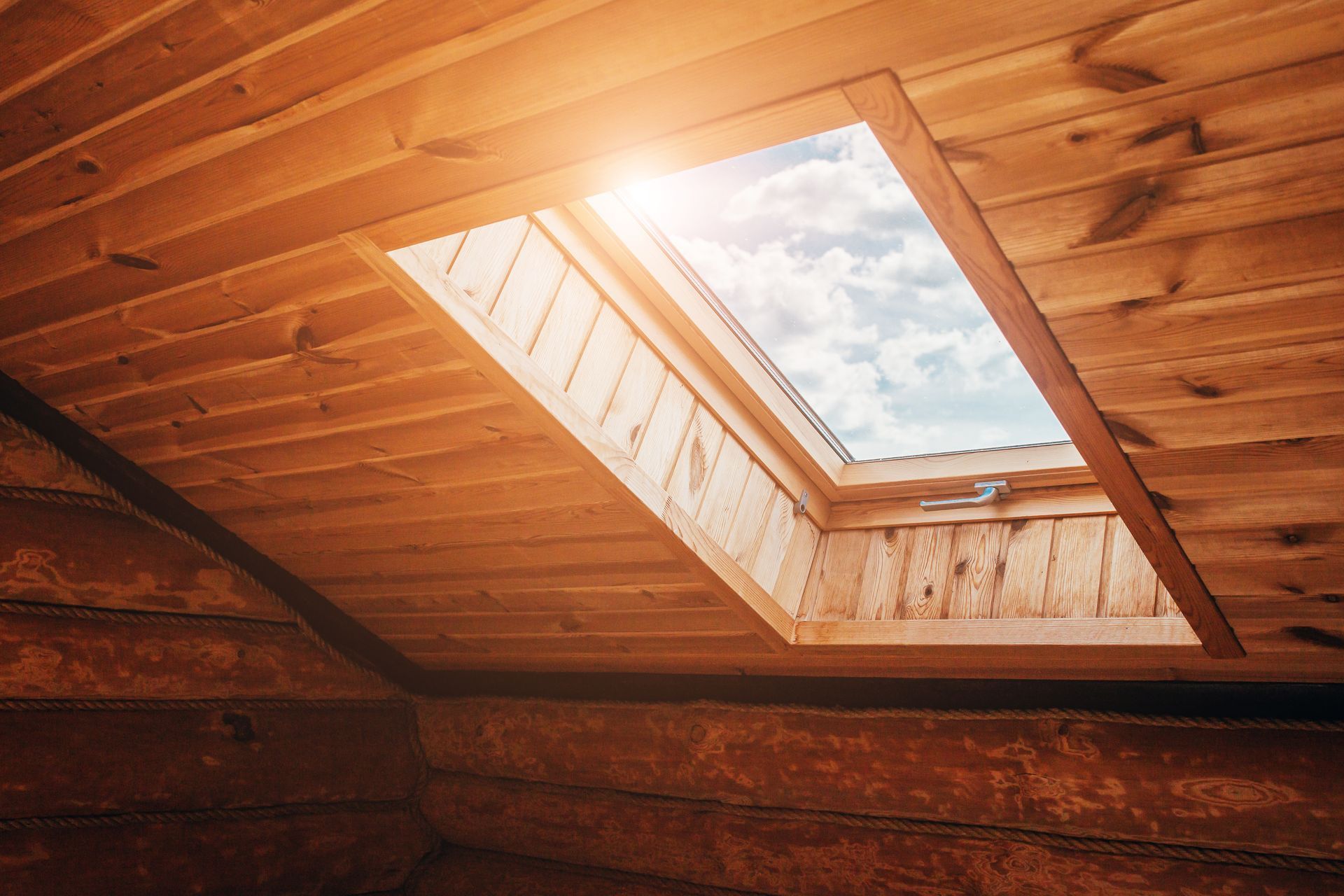 An inside view of a wood-panelled ceiling & a skylight with sunlight going through the window glass.