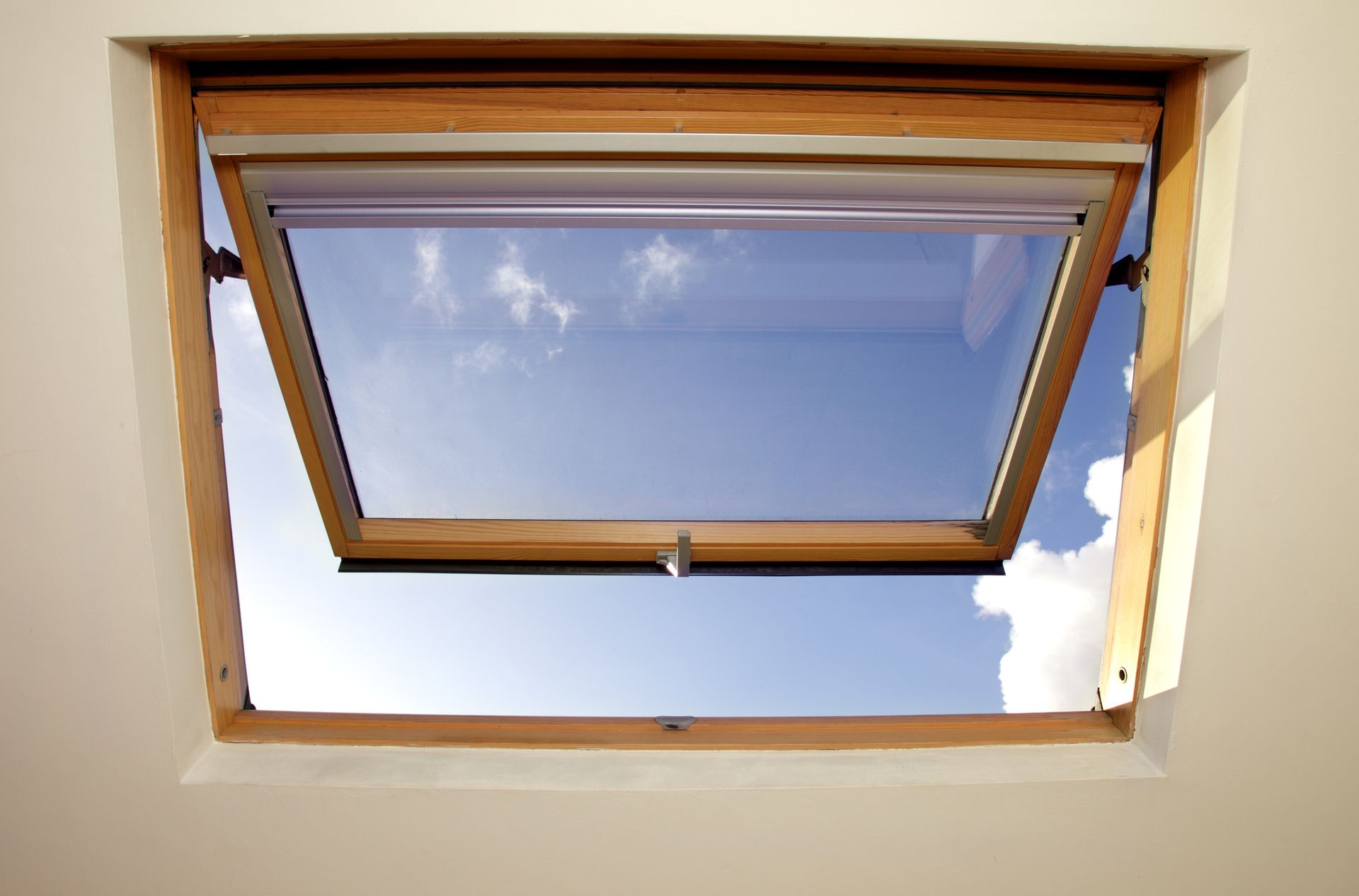 A skylight window, open to a sunlit blue sky.