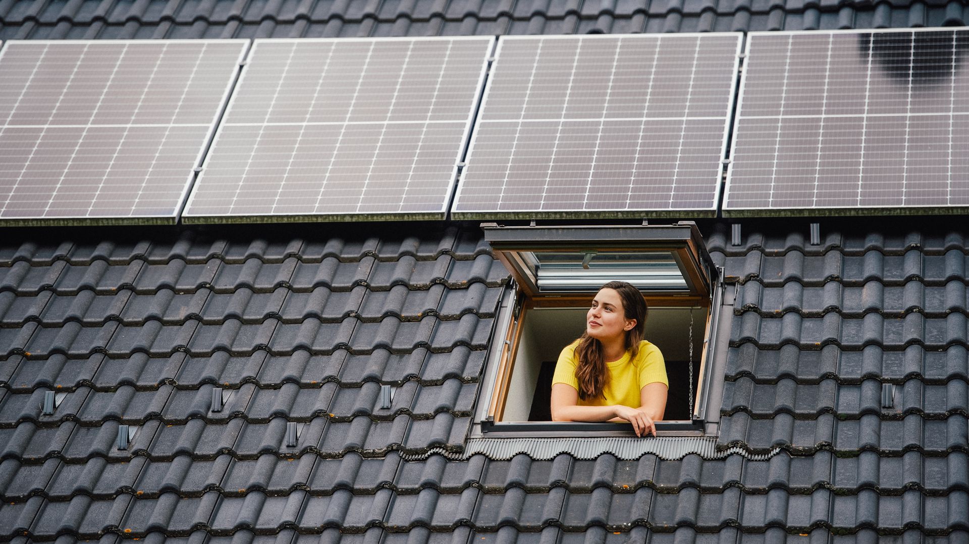 Woman looking out from modern roof skylights under solar panels on black tile rooftop. Woman looking out from modern roof skylights under solar panels on black tile rooftop.