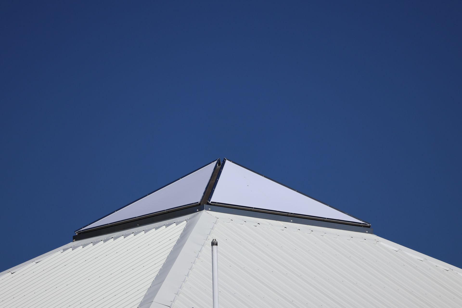 White rooftop with a pyramid-shaped top against a clear blue sky.