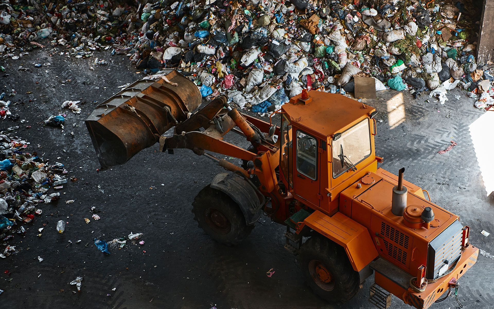 Orange loader in a landfill, scooping up trash.