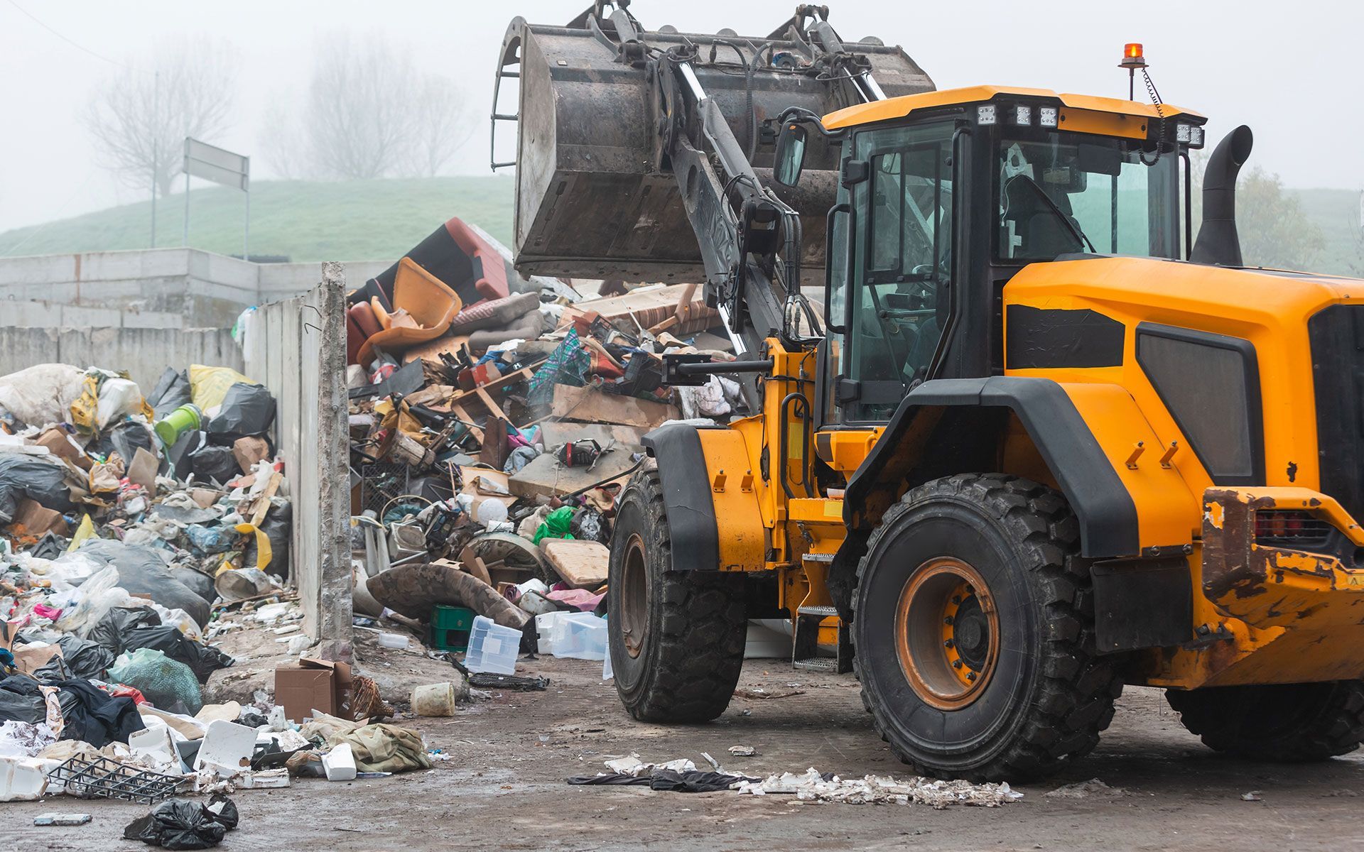Yellow bulldozer with a large bucket moving trash at a landfill.