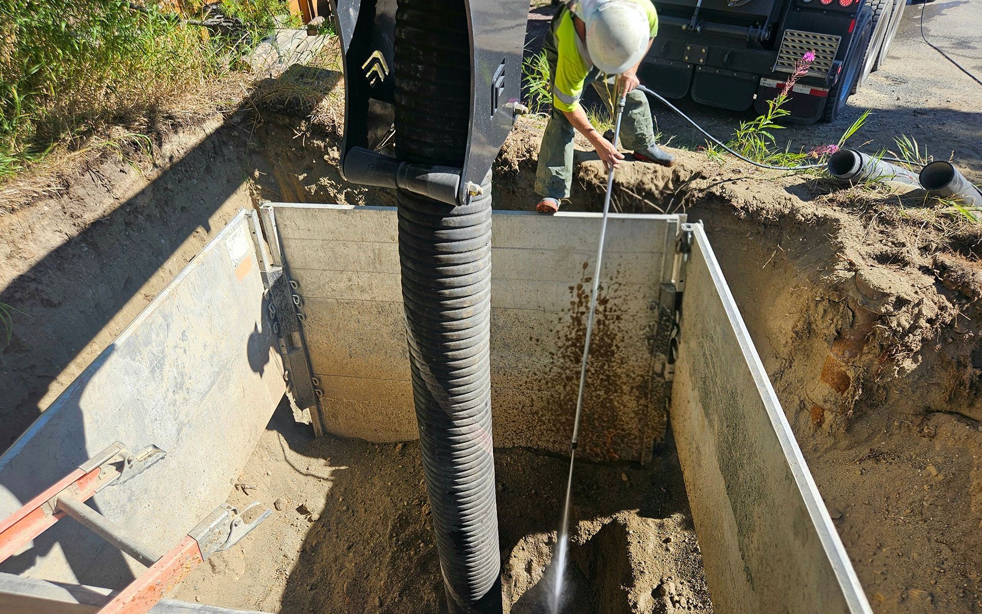 Construction worker in trench with corrugated pipe, metal walls, and tools.