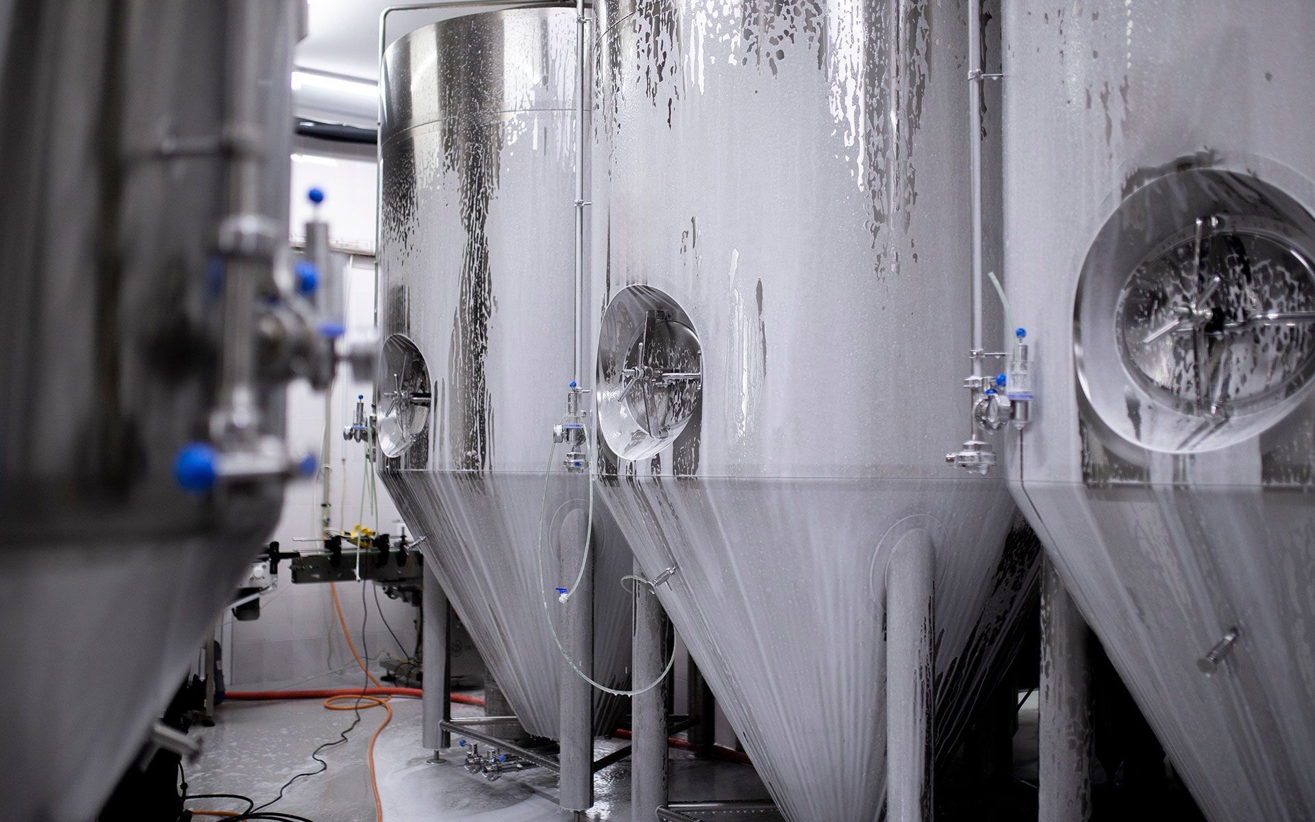 Stainless steel fermentation tanks in a brewery, covered in condensation.
