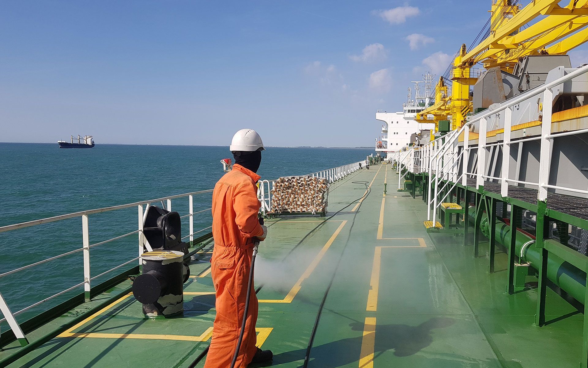 A person in an orange jumpsuit on a ship deck spraying water. The sea is visible in the background.