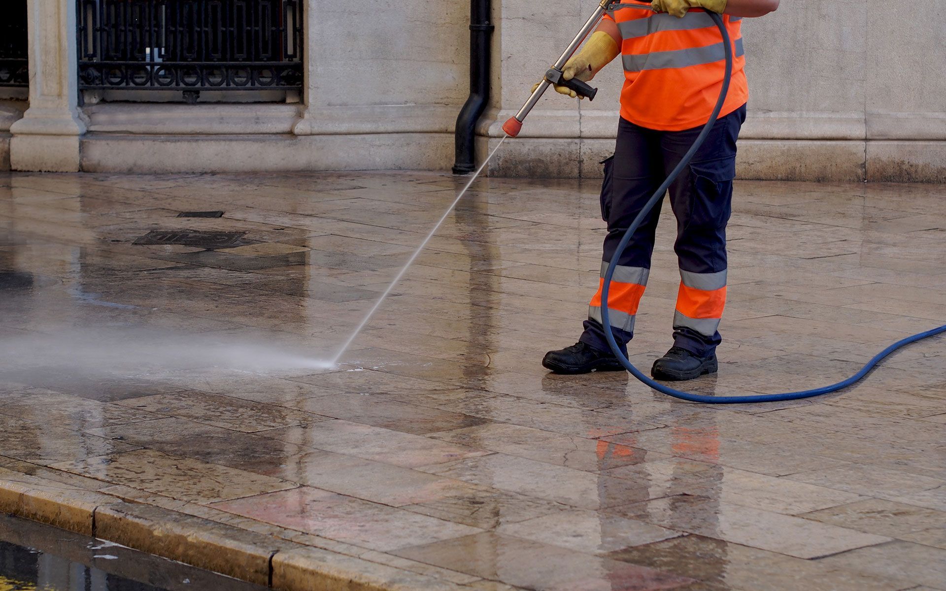 Man in orange vest power washing a sidewalk.