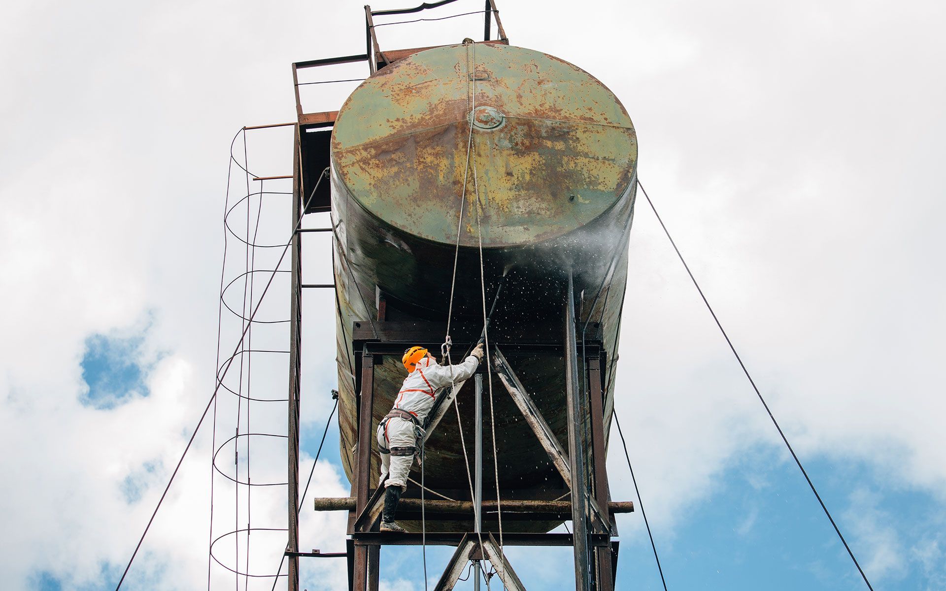 Person in protective suit inspecting a water tank, water spraying out.