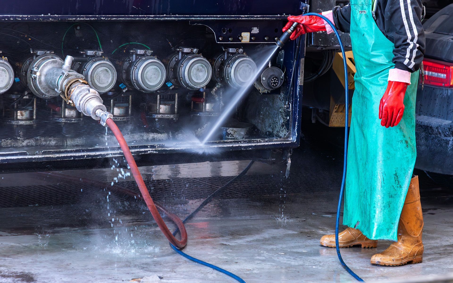 Person in protective gear washes truck fuel tanks with a hose.