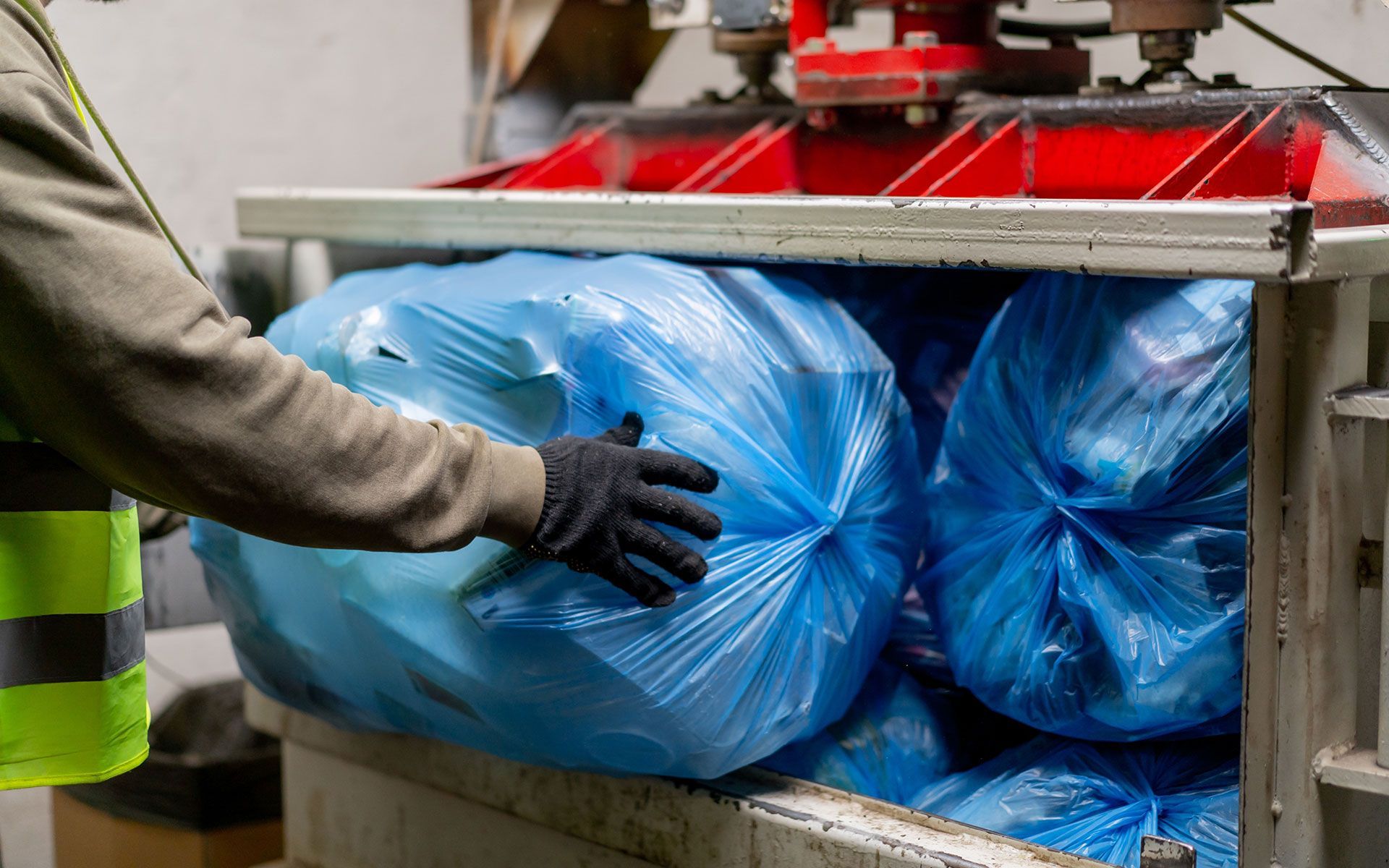 Worker handling blue trash bags in a machine.
