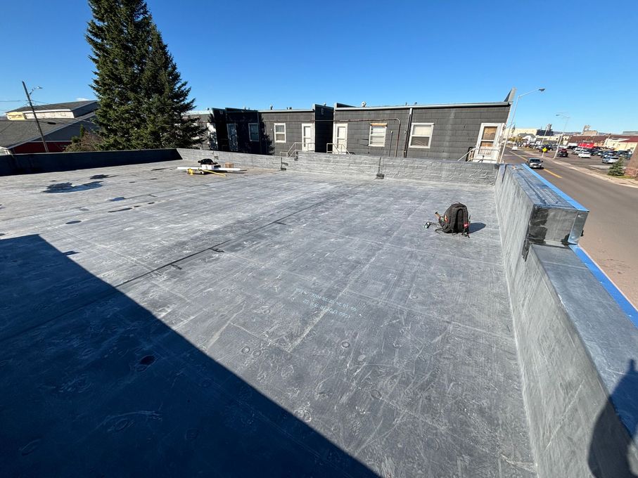 A flat, gray rooftop with a dark building in the background. The sky is blue.