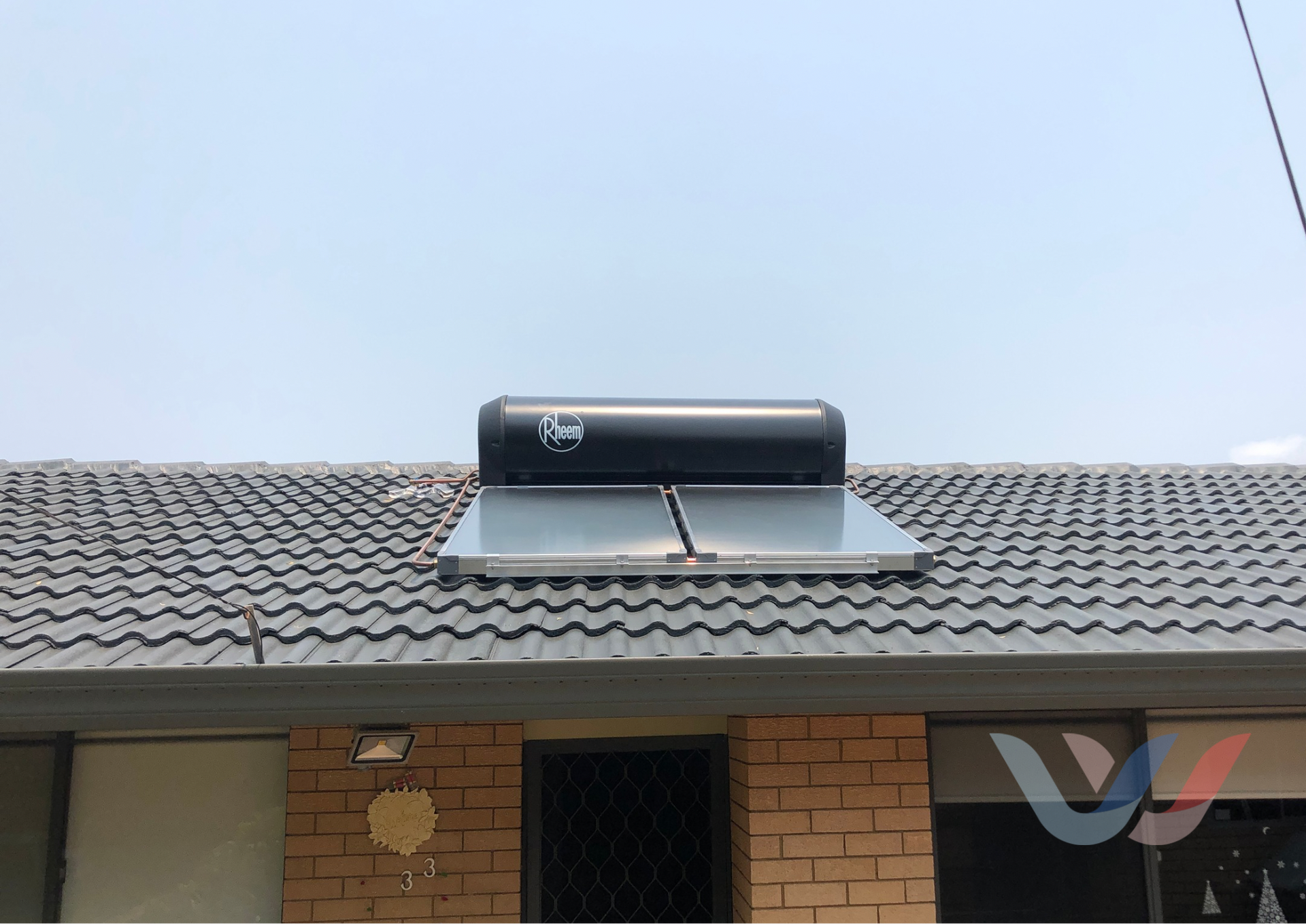 Solar Water Heater on a Tiled Roof Against a Blue Sky — Illawater Hot Water Services in East Corrimal, NSW