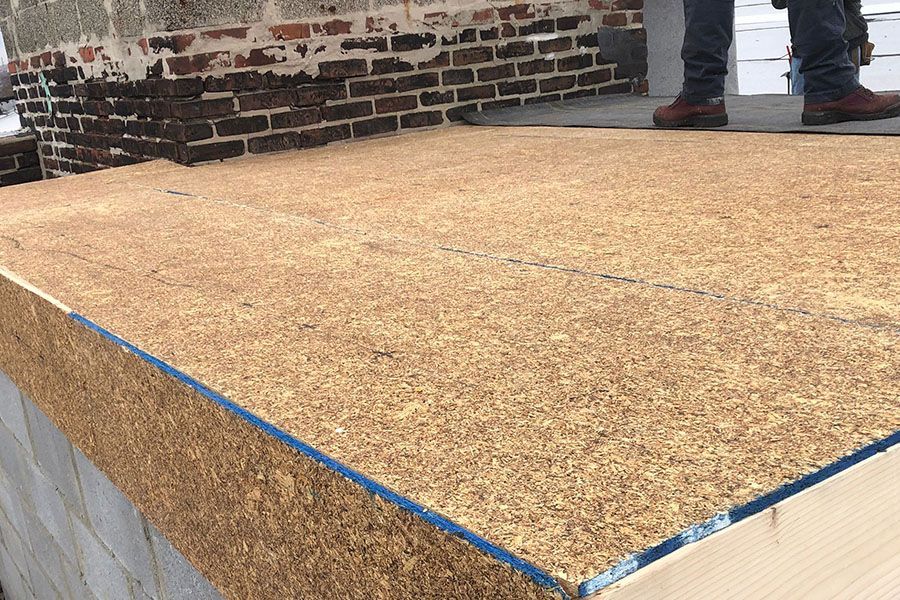 A person is standing on a wooden platform in front of a brick wall.