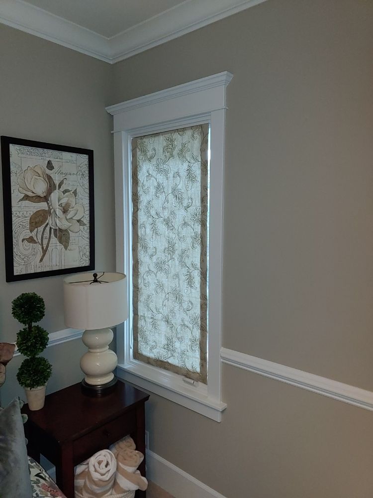 A bedroom with a lamp , nightstand , picture on the wall and a window.