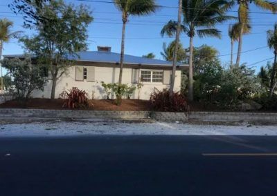 A white house with a blue roof is surrounded by palm trees.