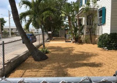 A chain link fence surrounds a lush green yard in front of a house.