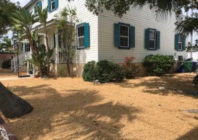 A white house with blue shutters and a lot of dirt in front of it.