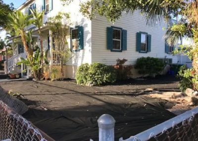A white house with blue shutters is behind a chain link fence