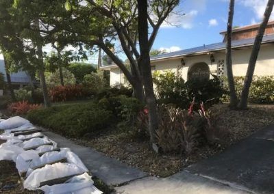 A row of sandbags are sitting on the sidewalk in front of a house.