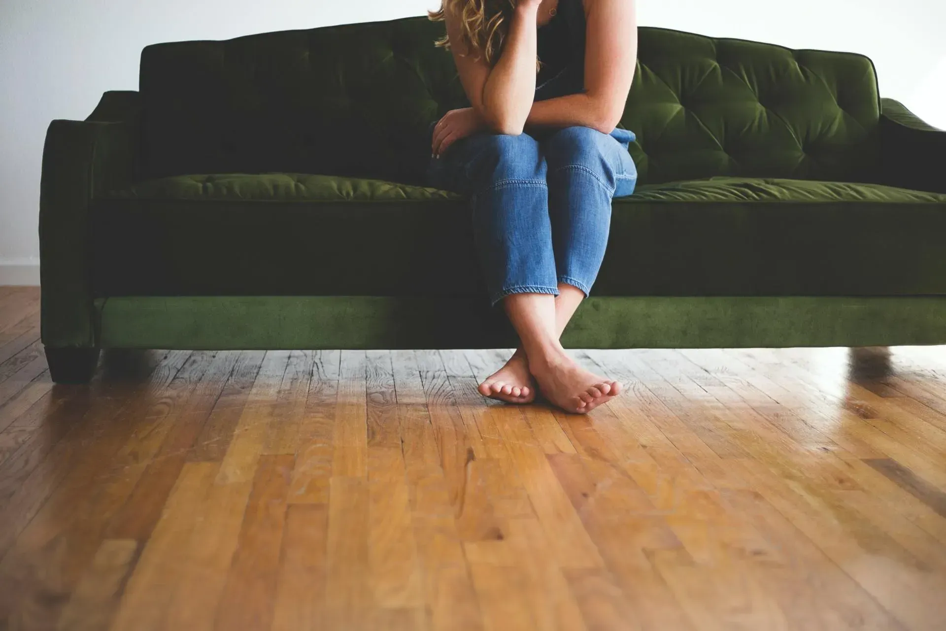 A woman is sitting on a green couch on a wooden floor