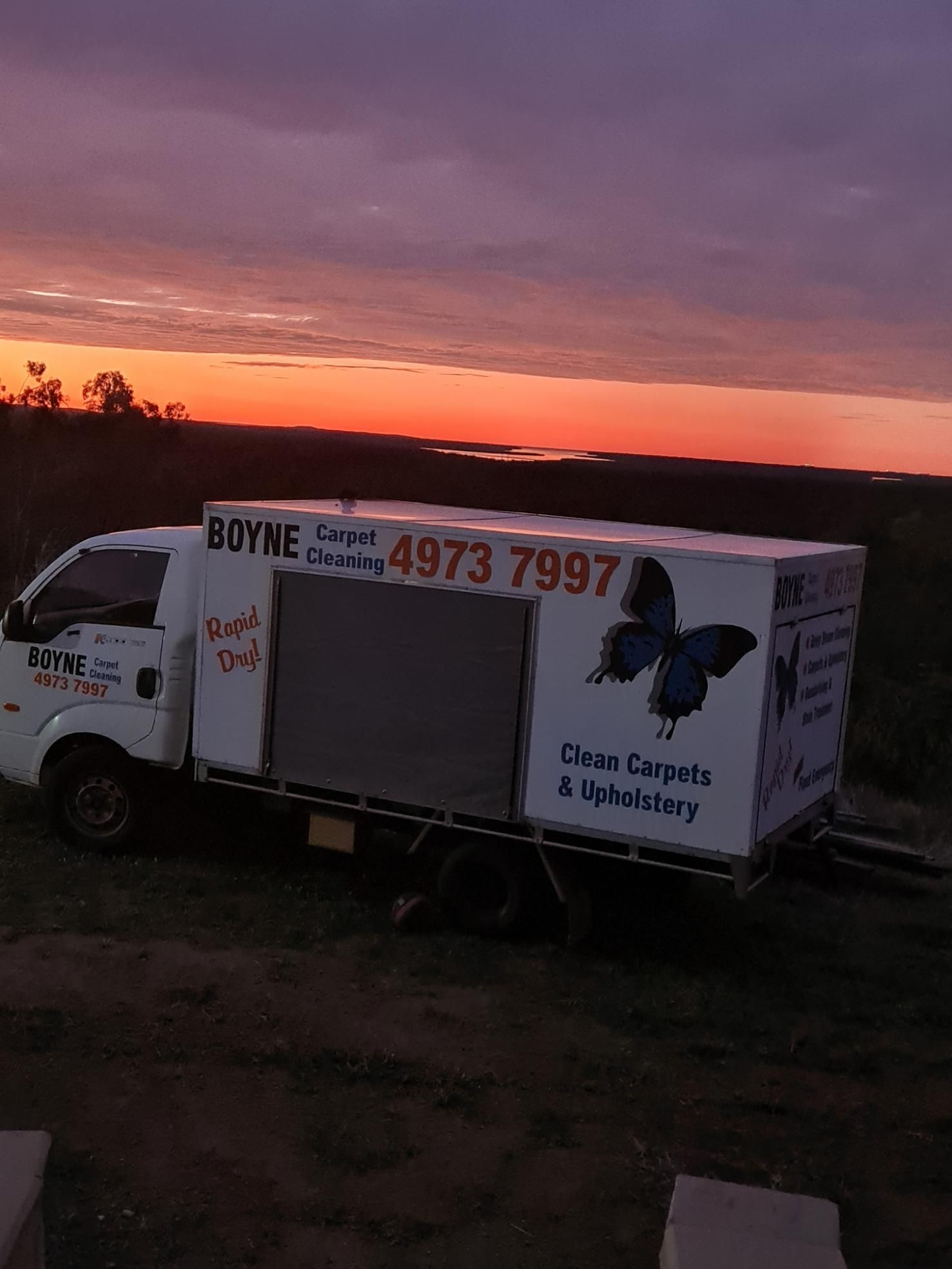White Truck With a Butterfly on the Side is Parked in a Field at Sunset — Boyne Carpet Cleaning in Iveragh, QLD