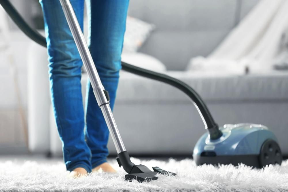 Woman is Vacuuming a White Carpet in a Living Room — Boyne Carpet Cleaning in Iveragh, QLD