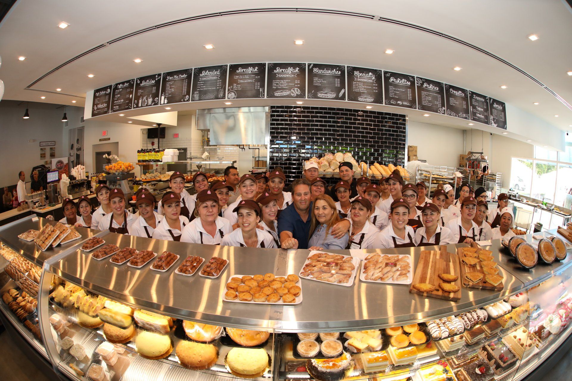 Bakery staff pose behind display of baked goods, man and woman in the center, shop interior.