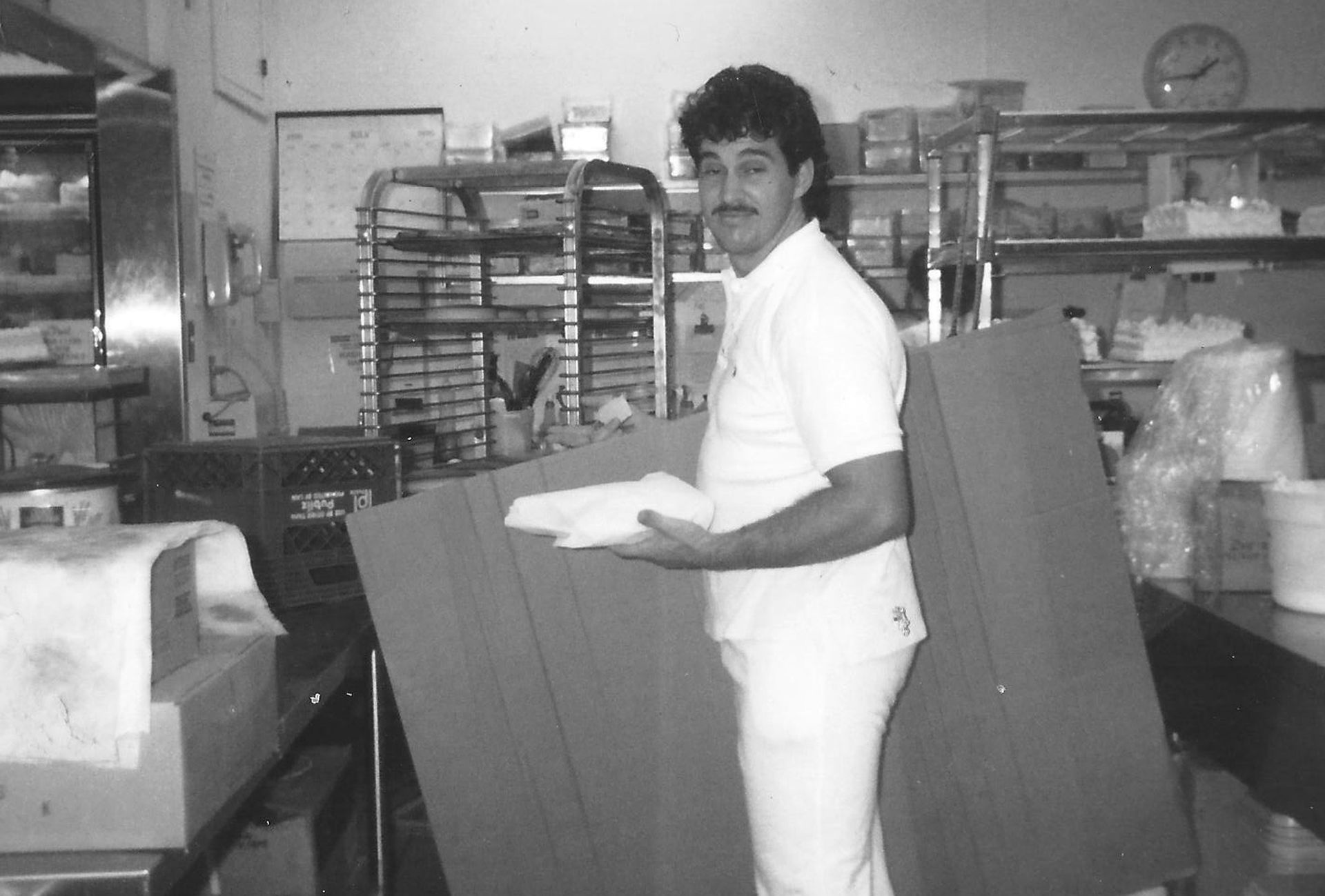 Juan Montano in white uniform holds folded towels in a commercial kitchen, smiling.