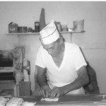 Baker in white hat and t-shirt, rolling dough at a bakery counter.