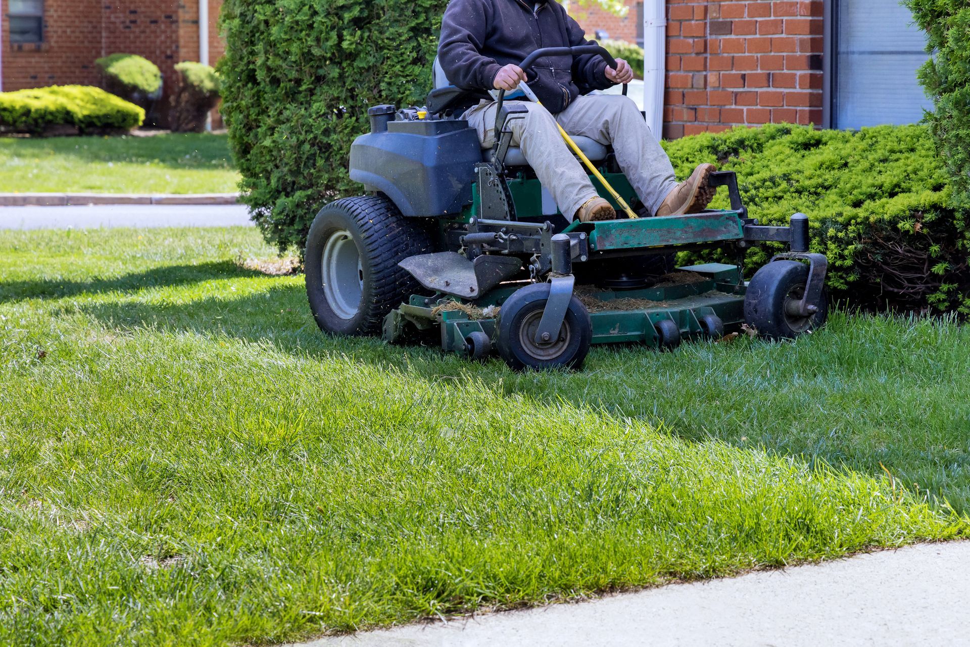 Person mowing lawn with a riding mower on a sunny day.