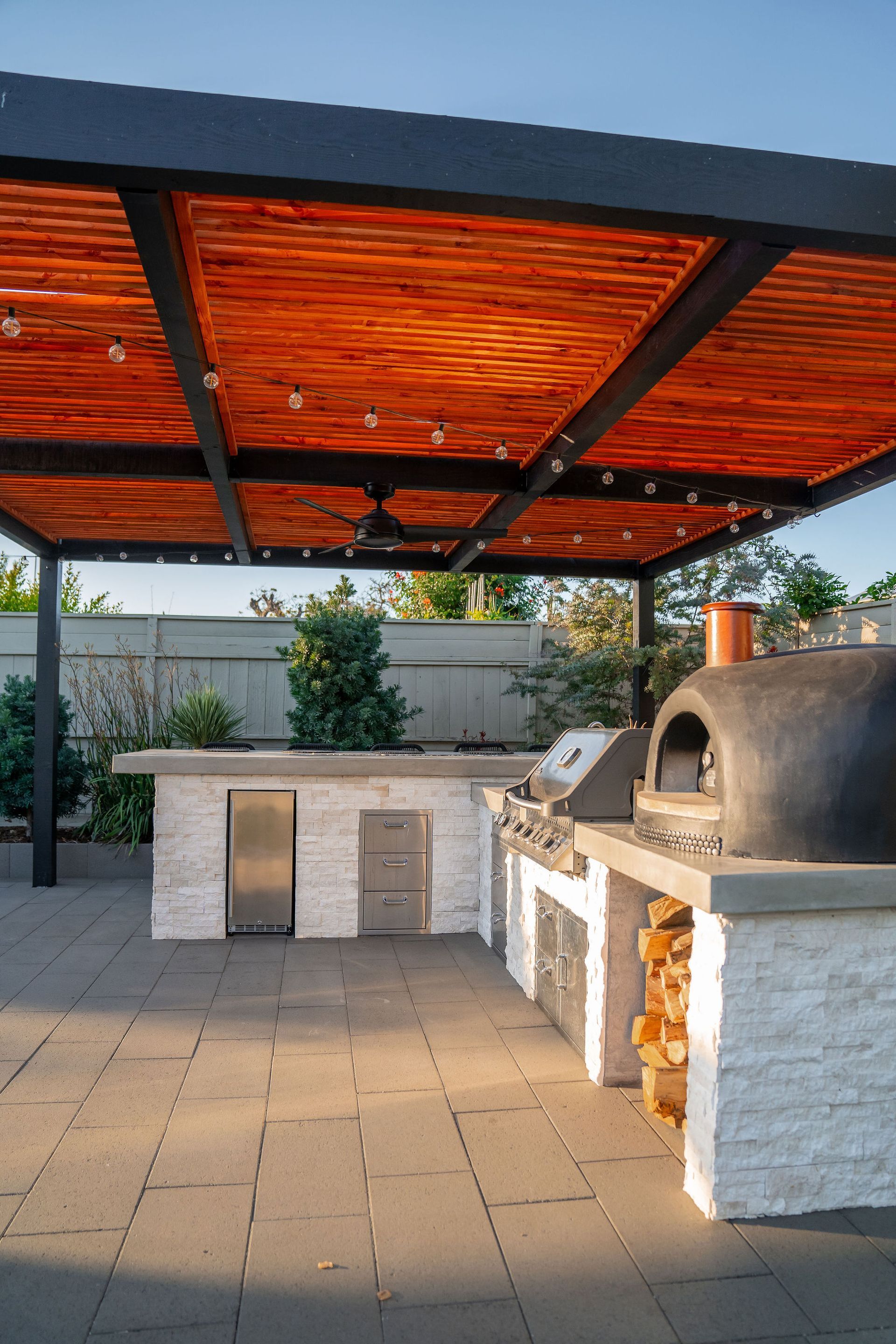 Outdoor kitchen with a brick pizza oven and a wood-covered pergola.