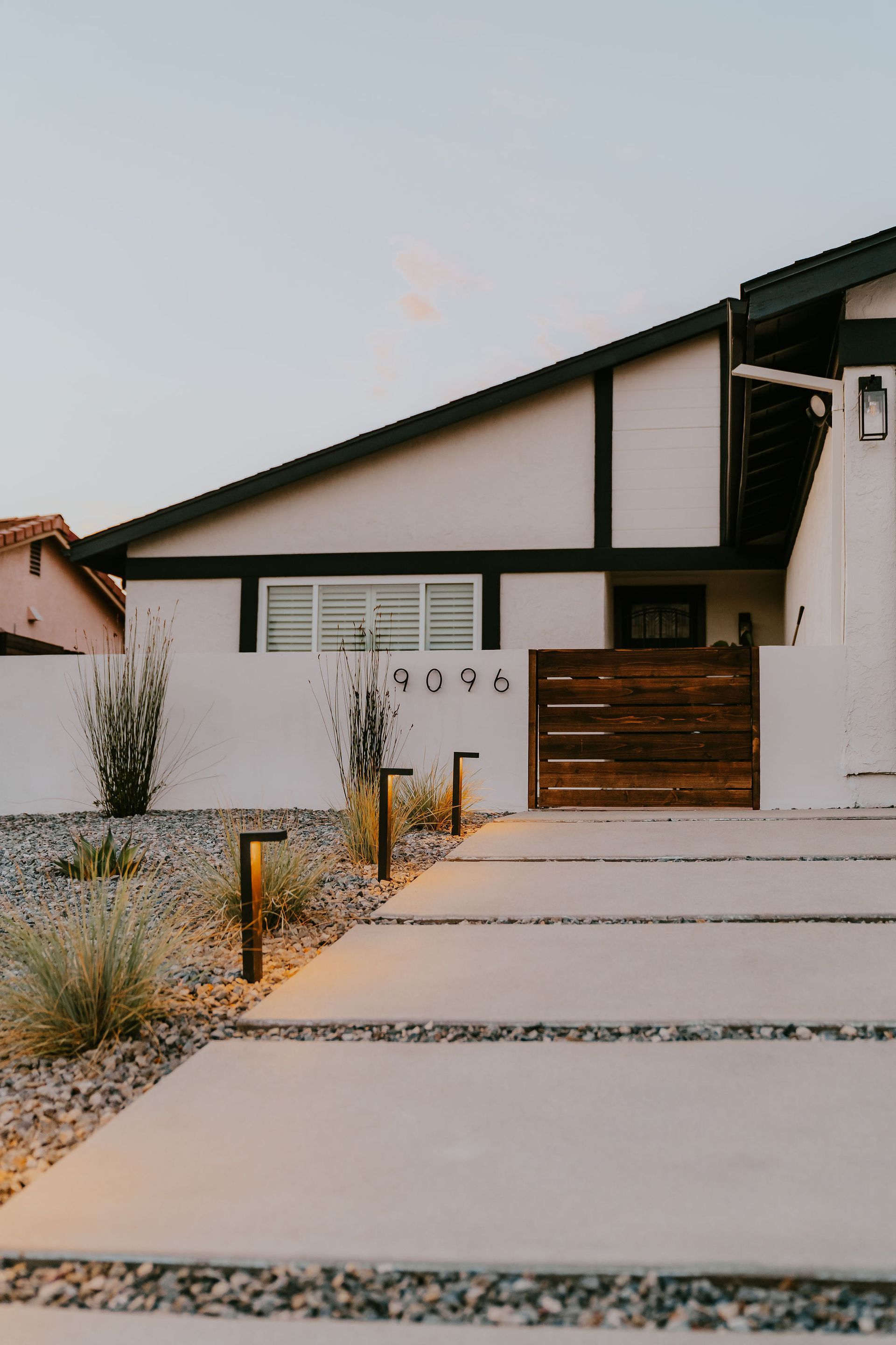 Modern home exterior with concrete pathway and wooden gate. Dusk lighting.