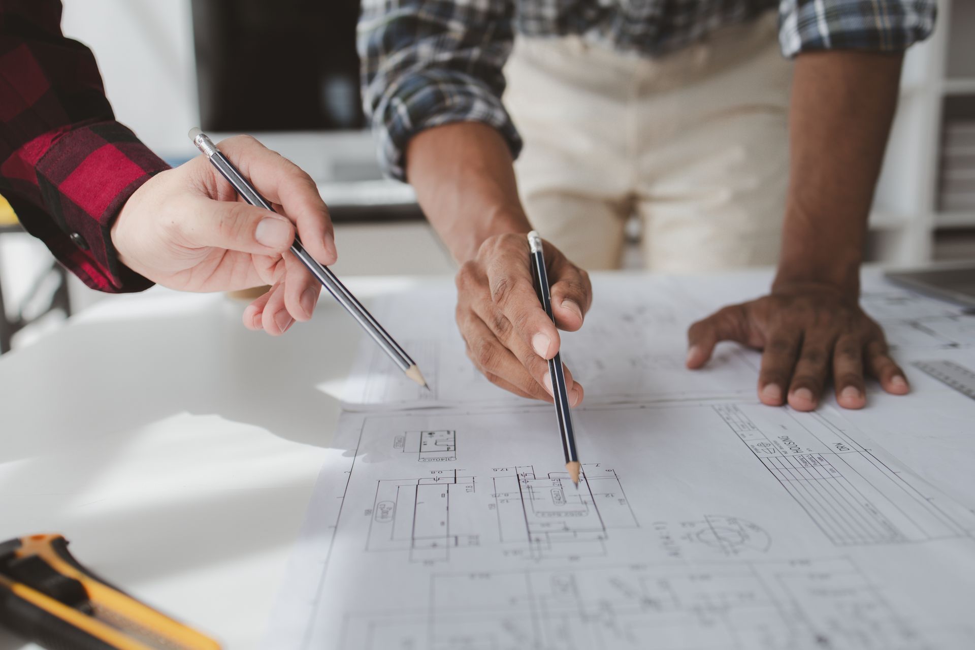 Two people with pencils pointing at architectural blueprints on a white table.