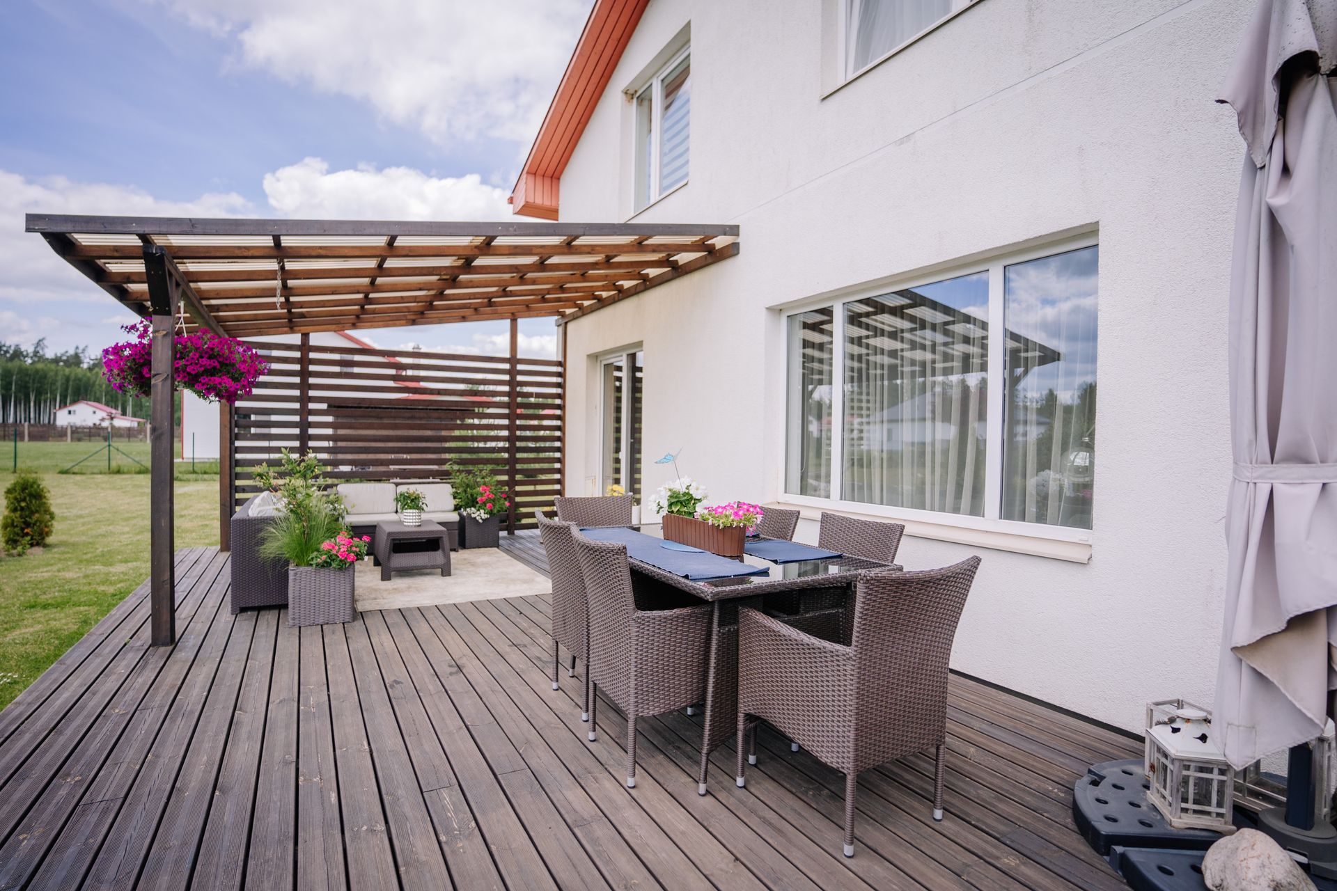 Wooden deck with outdoor dining table and seating, attached to a white house with pergola.