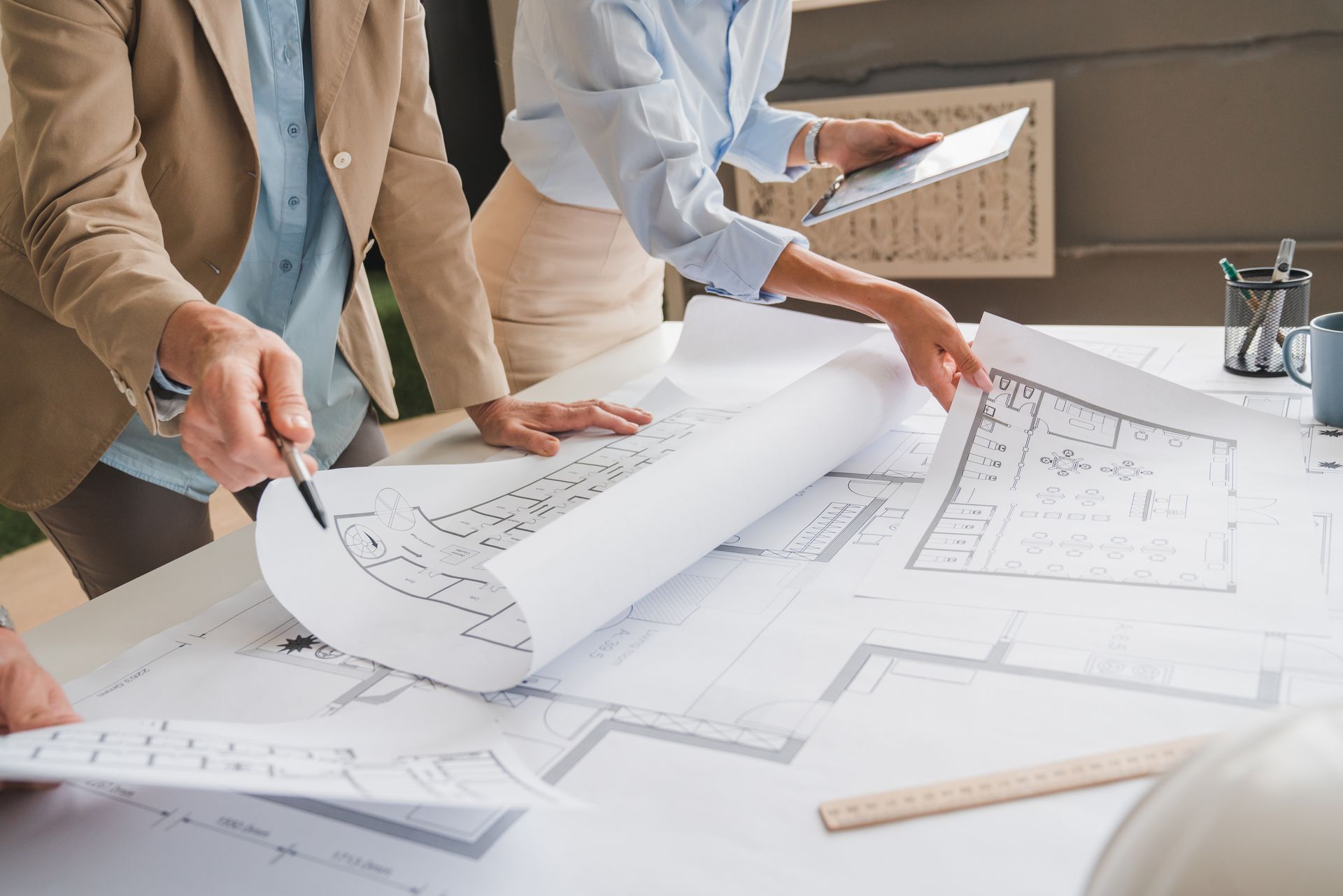 People reviewing architectural blueprints at a table, pointing, and holding a tablet.