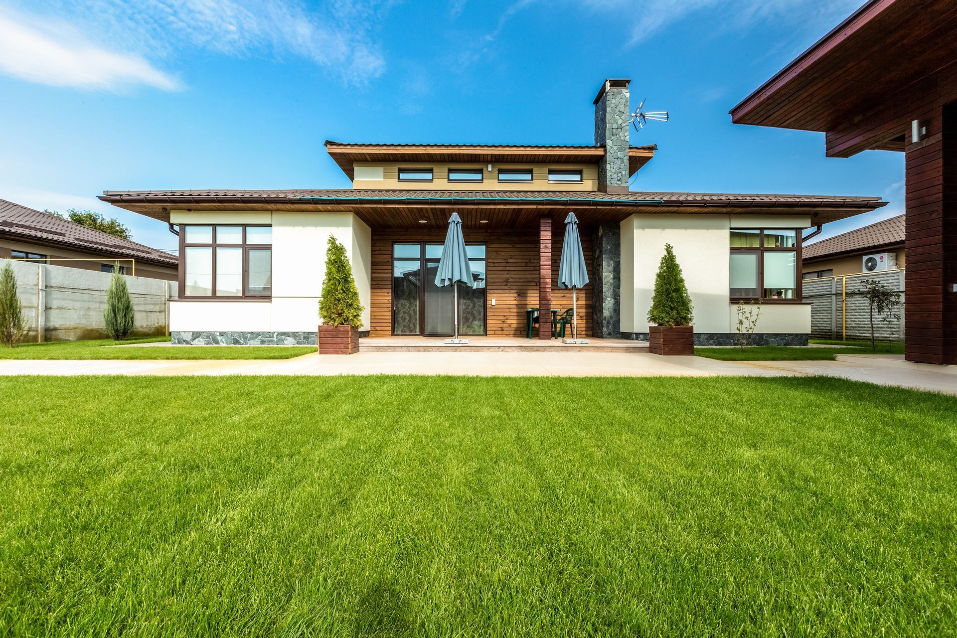Modern house with a green lawn, blue sky, and two small trees.