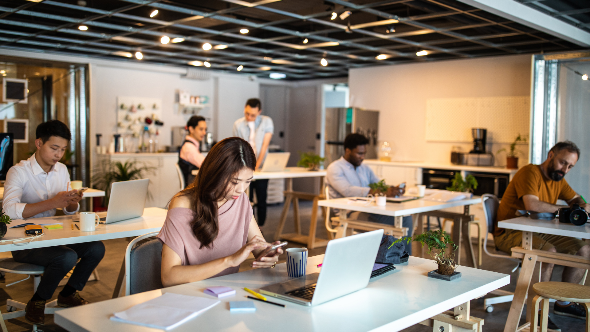 People working on laptops in a modern open office with desks and warm lighting