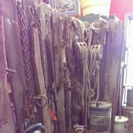 An assortment of vintage farm tools, including chains and wooden pulleys, hanging against a weathered wooden wall.