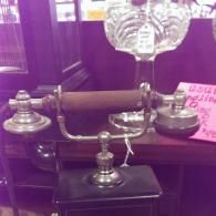 An antique metal candlestick telephone with a brown handle, sitting on a dark base in a shop setting.