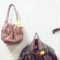 Two handbags with price tags hang on a white pegboard wall.