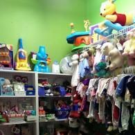 Shelves filled with various toys, baby clothes, and a plush Winnie the Pooh against a vibrant green wall.
