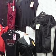 A display of various shirts and tops on hangers and a mannequin, featuring dark colors and a red garment with tags.