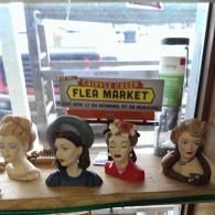 Four decorative female head vases sit on a shelf in front of a 