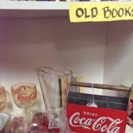 A Coca-Cola caddy with a matching glass and pitcher on a shelf labeled 