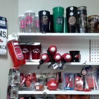 A retail display shelf featuring Arkansas Razorbacks branded cups, mugs, and various sports merchandise in red and black.