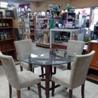 A glass-topped dining table with four light-colored upholstered chairs inside a retail store.