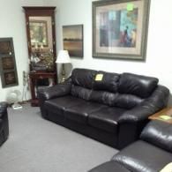 A dark brown leather sofa in a room with a tall wooden mirror, a table lamp, and two framed wall pictures.