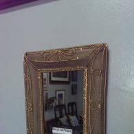 A rectangular, antique-style mirror with an ornate, bronze-colored metal frame mounted on a light gray wall.