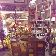 A cluttered, rustic shop interior featuring a wooden cabinet with many small drawers filled with flowers and retail items.